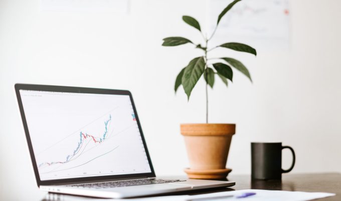 workplace of stock trader with laptop in minimalistic style. Working Desk of investment manager with with green plant and cup of coffee. stocks price rising graph data trend laptop screen.